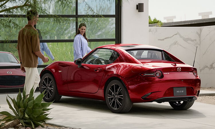 Soul Red Crystal Metallic MX-5 RF with the top up parked in front of mirrored garage door, a smiling couple approach each door.