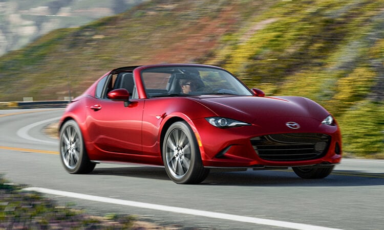 Soul Red Crystal Metallic MX-5 RF with the top down drives around a bend on a verdant escarpment road.