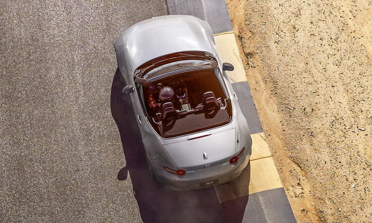 Top-down view of professional driver in Machine Grey Metallic   MX-5 with the top down taking a right turn on a racetrack.