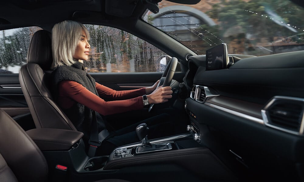Passenger side view of woman driving in Mazda CX-5 with rain outside window.