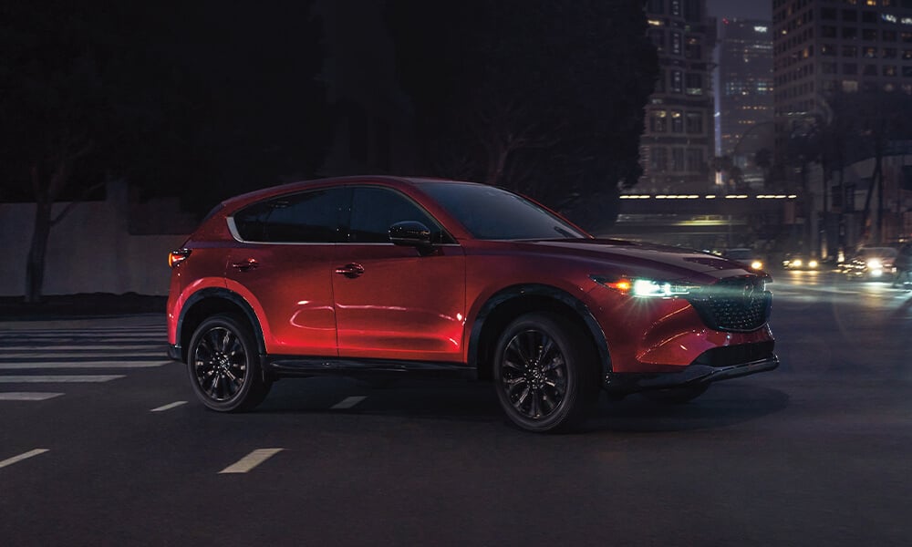 Side view of Soul Red Crystal Mazda CX-5 entering city intersection at night.
