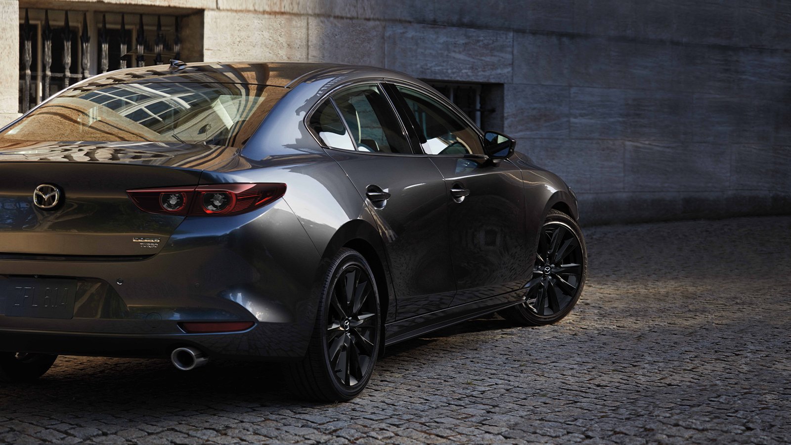 Une Mazda3 platine garée dans la rue.