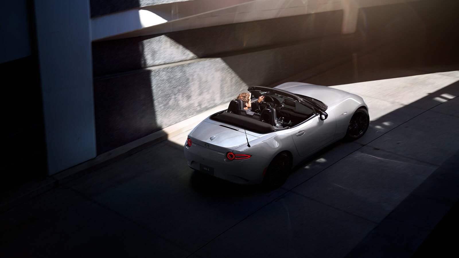 A person drives an MX-5 ST with the top down in the city.