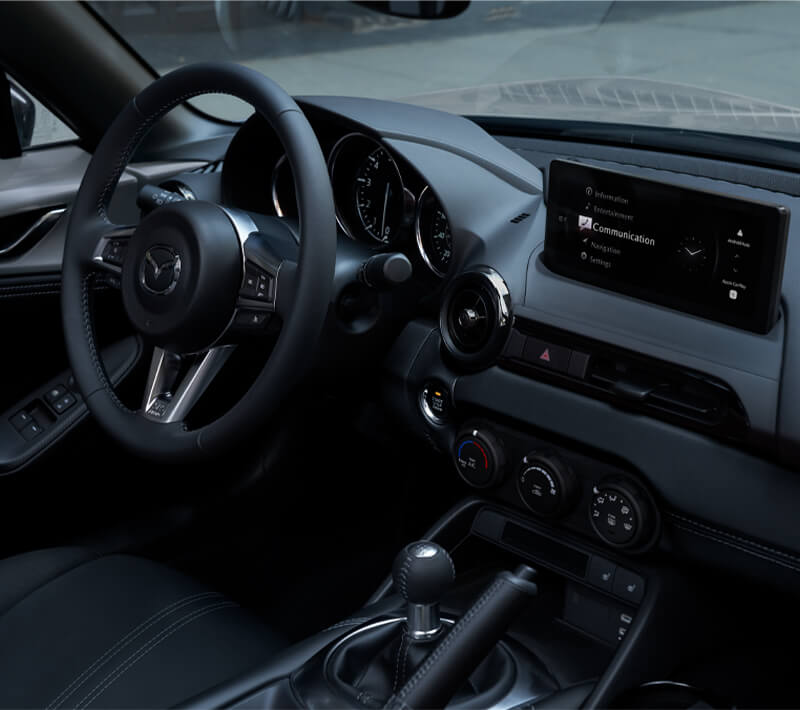 Interior view of the MX-5 ST driver’s side seat with steering wheel and dashboard featuring black leather trim details.