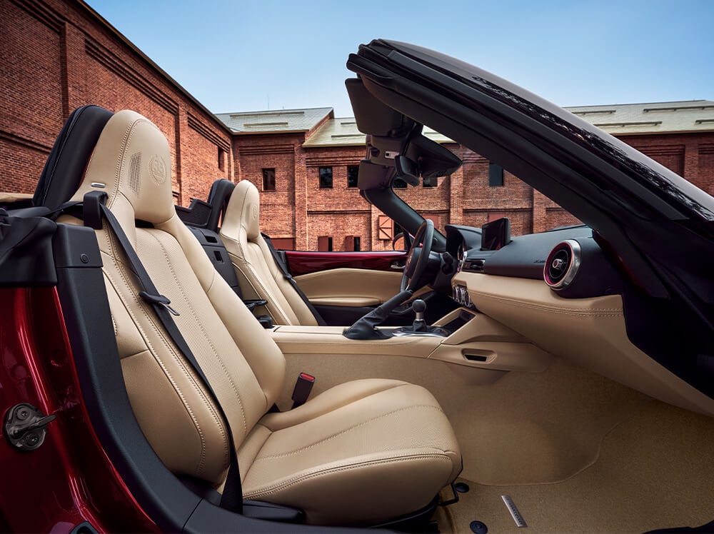 View from the passenger side of the MX-5 ST 35th Anniversary Edition with its top down in front of a building. 