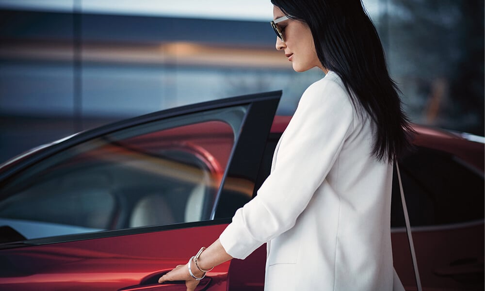Une femme ouvre la portière côté conducteur d’un Mazda CX-30 rouge vibrant cristal métallisé