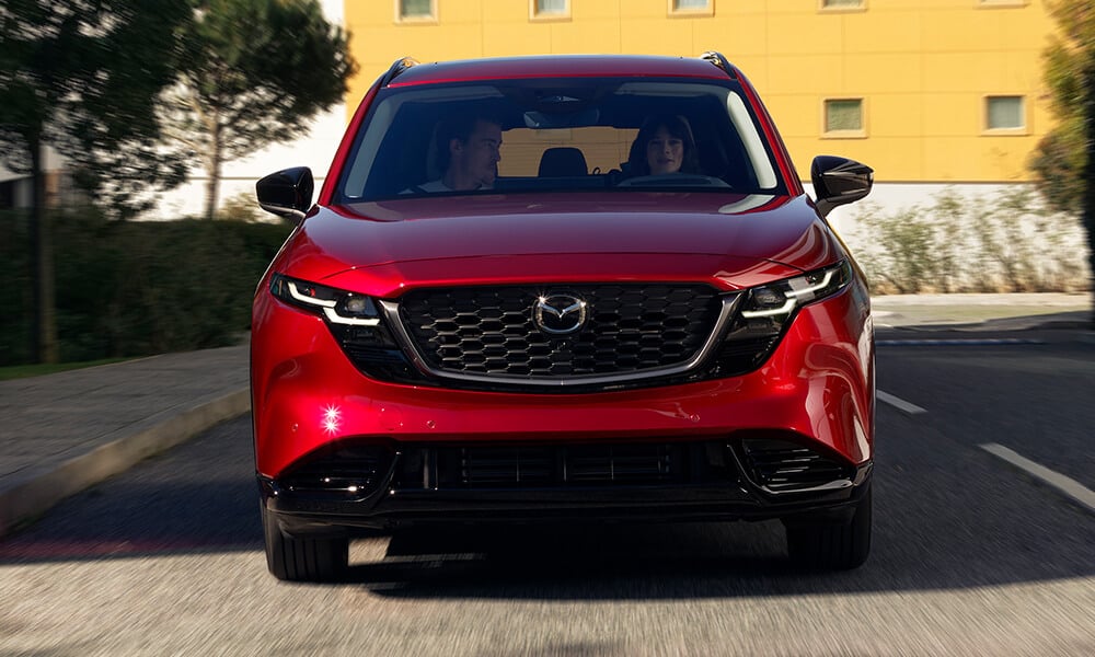 Low-angle front view of a Soul Red Crystal Metallic Mazda CX-5 driving on a road.