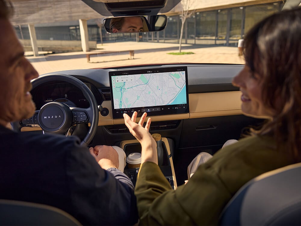 Vue de l’arrière de deux personnes dans les sièges avant avec l'écran central montrant la navigation Google Maps 