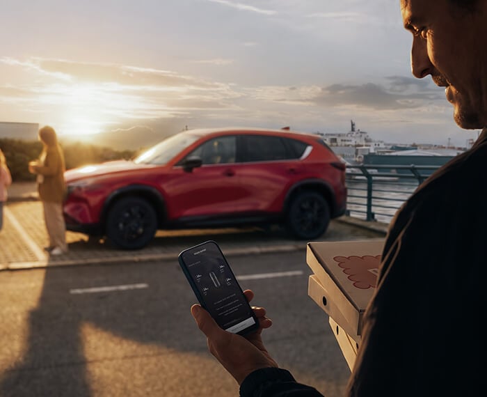 Man using his phone with a Mazda CX-5 parked near the waterfront in the background.
