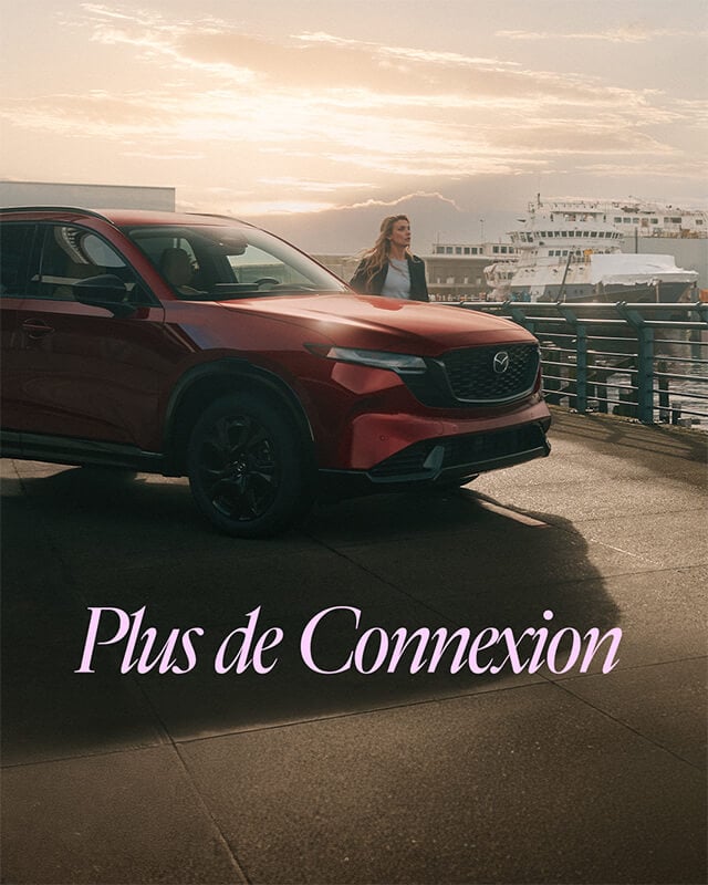 Un Mazda CX-5 stationné au bord de l’eau avec une femme debout à ses côtés.
