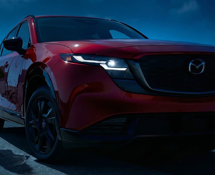 Low-angle front corner view of a Mazda CX-5 against a dark blue sky.