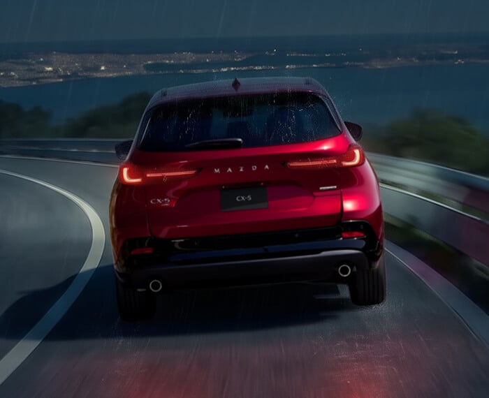 Rear view of a Mazda CX-5 driving on a winding road at night.