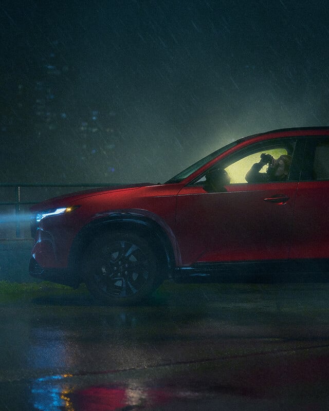 Side profile of a Mazda CX-5 driving on a misty road with headlights on.