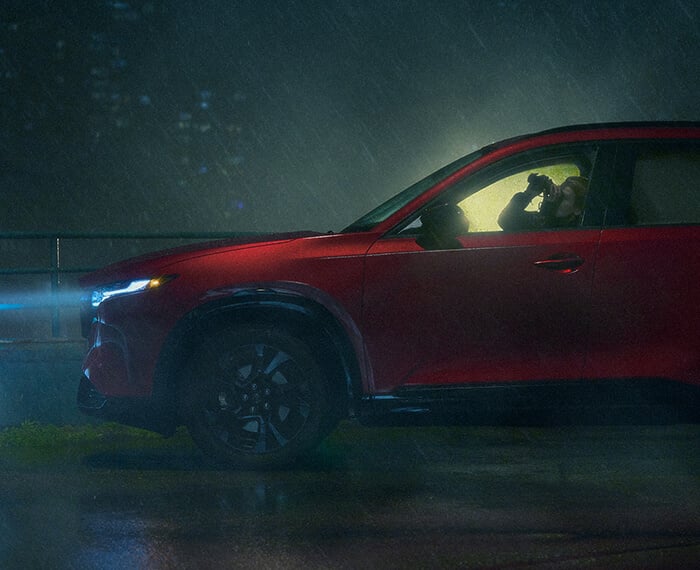 Side profile of a Mazda CX-5 driving on a misty road with headlights on.