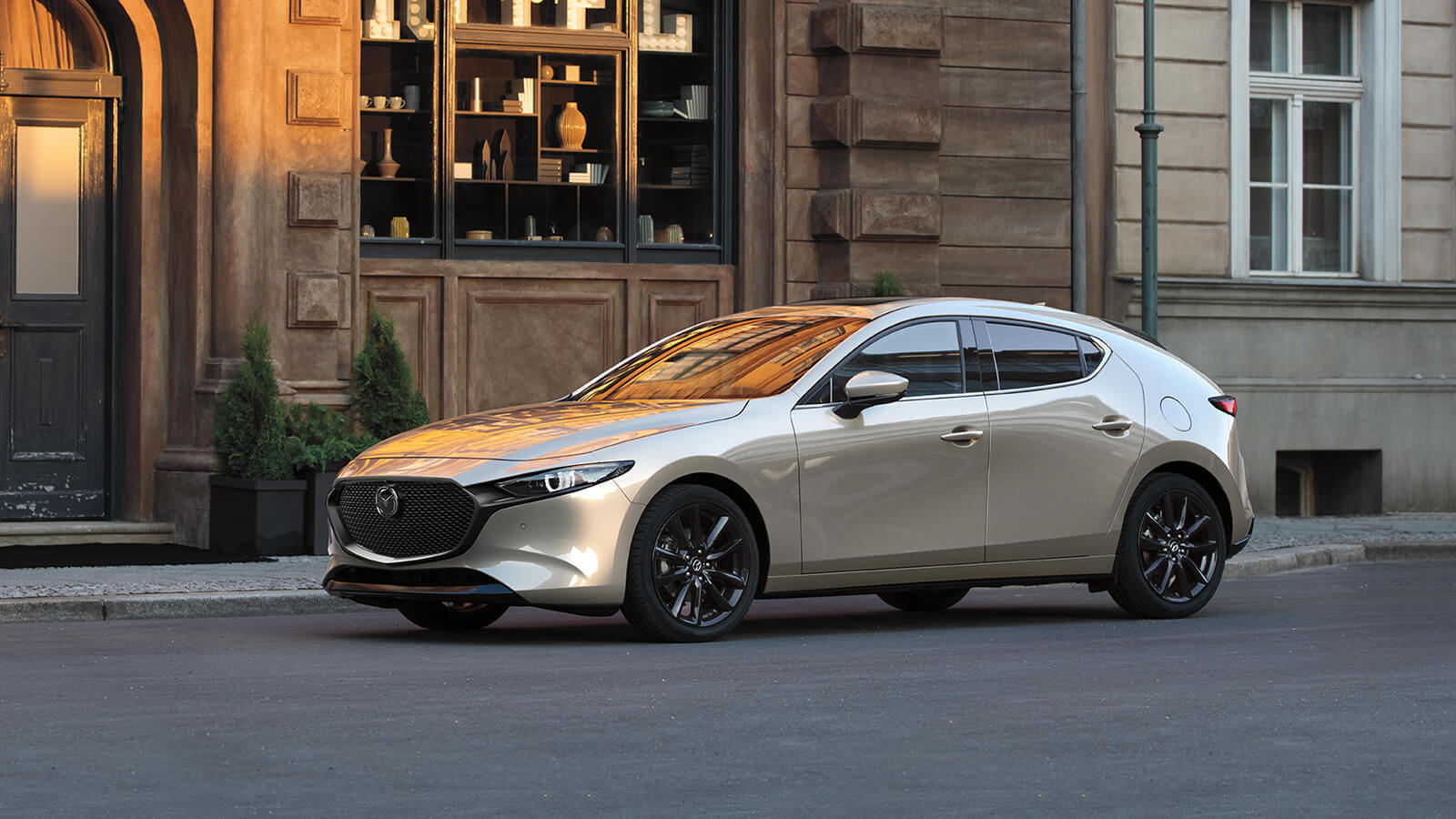 Vue de profil d’une Mazda3 Sport quartz platine métallisé stationnée sur une rue tranquille.