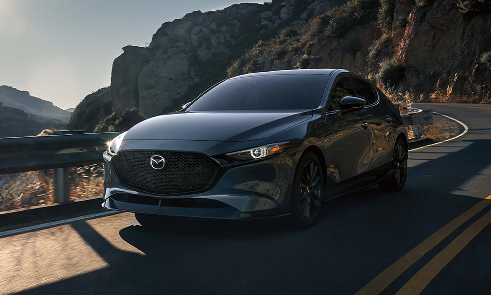 Vue de l’avant d’une Mazda3 Sport bleu cristal foncé mica sur une autoroute sinueuse.