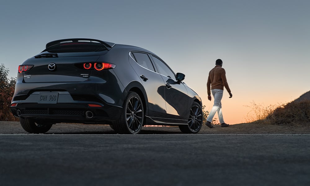 Vue de profil d’une femme portant des lunettes de soleil, à travers la fenêtre ouverte du côté passager, conduisant une Mazda3 Sport.