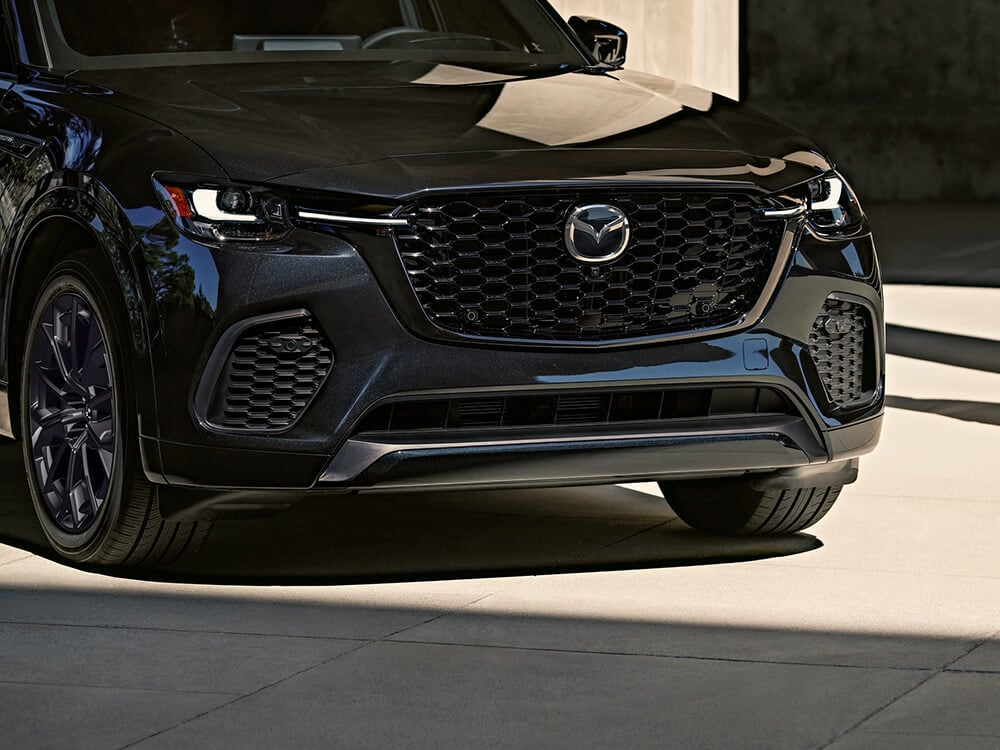 The front hood, grille and Mazda emblem of a Jet Black CX-70 reflect the daylight.